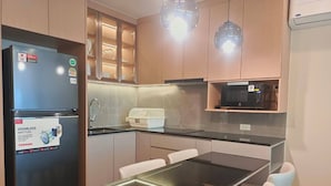 A modern kitchen with a built-in refrigerator, a microwave, and a glass-top dining table with chairs. - The Regent Residence Kamala (Kamala)