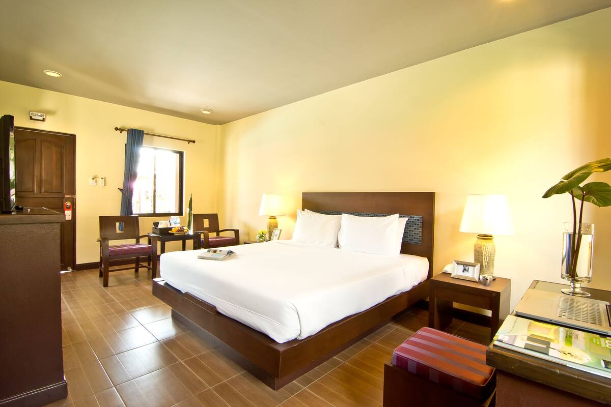 A hotel room with a large bed, two bedside tables with lamps, a chair, a desk, and a window with curtains.