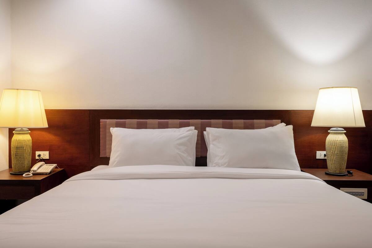 A hotel room with a large bed, two bedside tables with lamps, a telephone, and a power outlet.