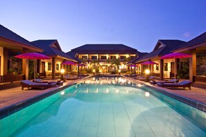 Piscina com espreguiçadeiras e guarda-sóis, cercada por edifícios com telhado de azulejos.
