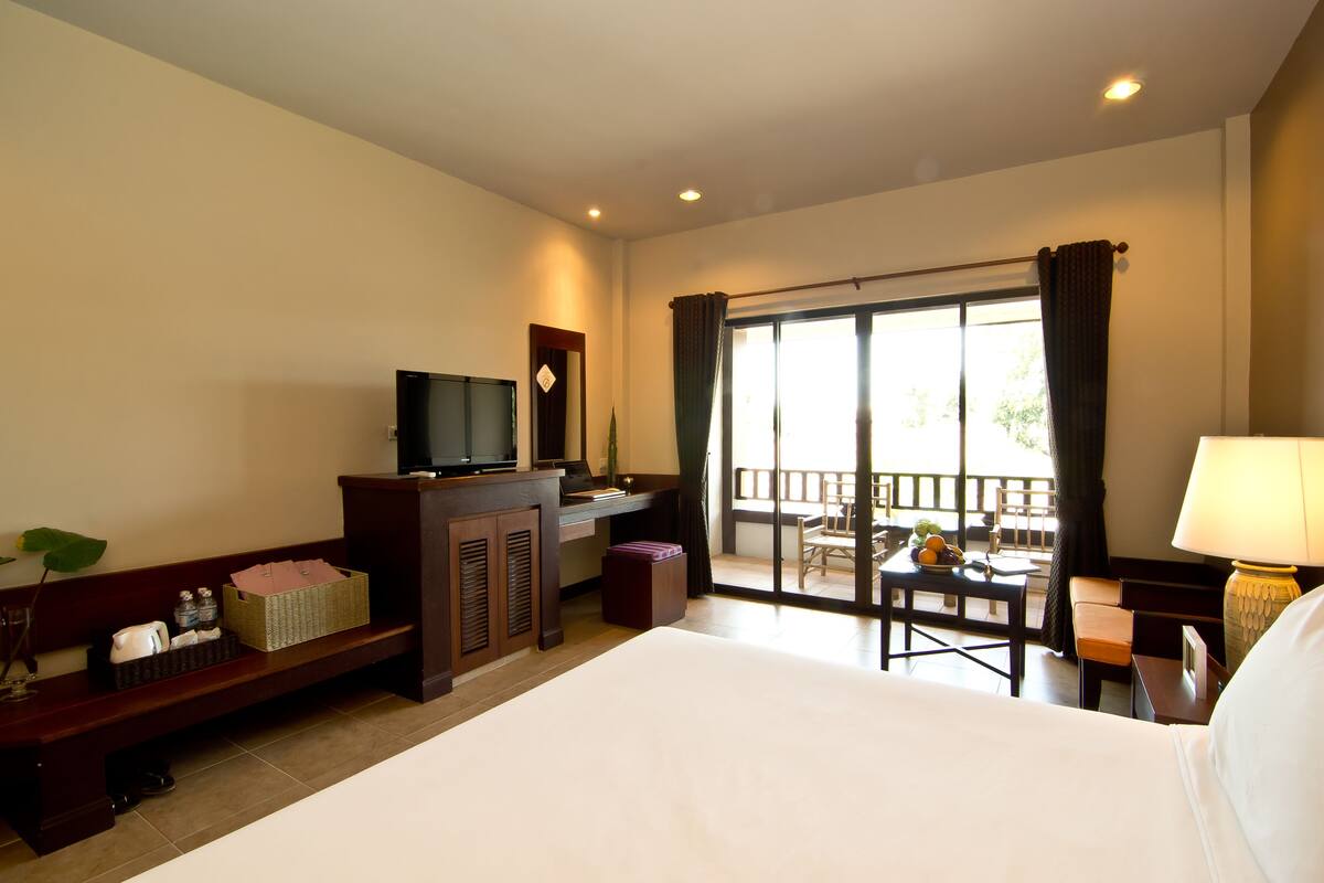 A hotel room with a bed, a desk, a television, a chair, and a balcony with a view.