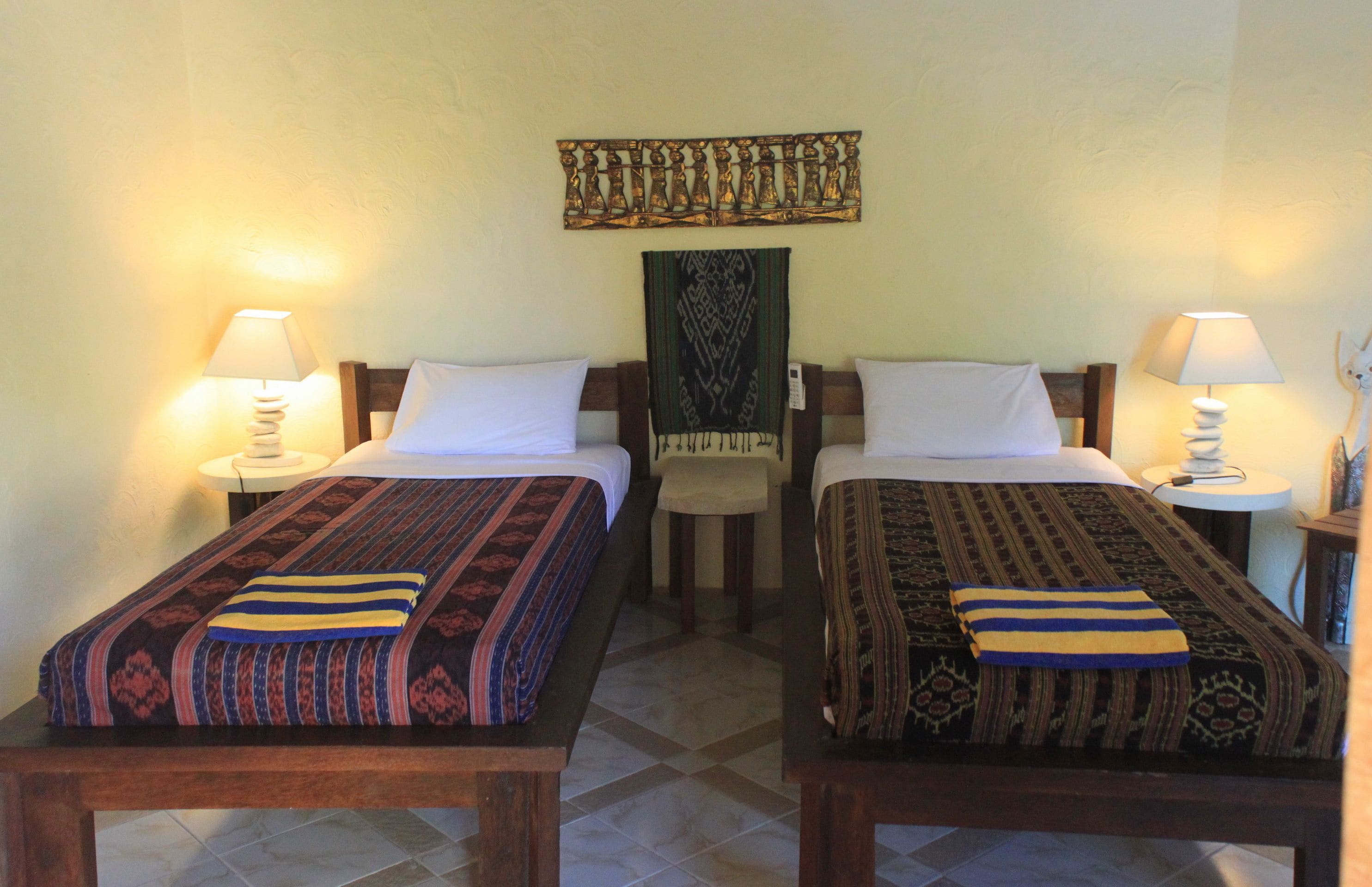 Deux lits simples avec des couvre-lits à motifs, une tapisserie murale et deux lampes de chevet.