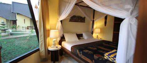 A bedroom with a bed, two bedside lamps, a window with curtains, and a view of the outside.