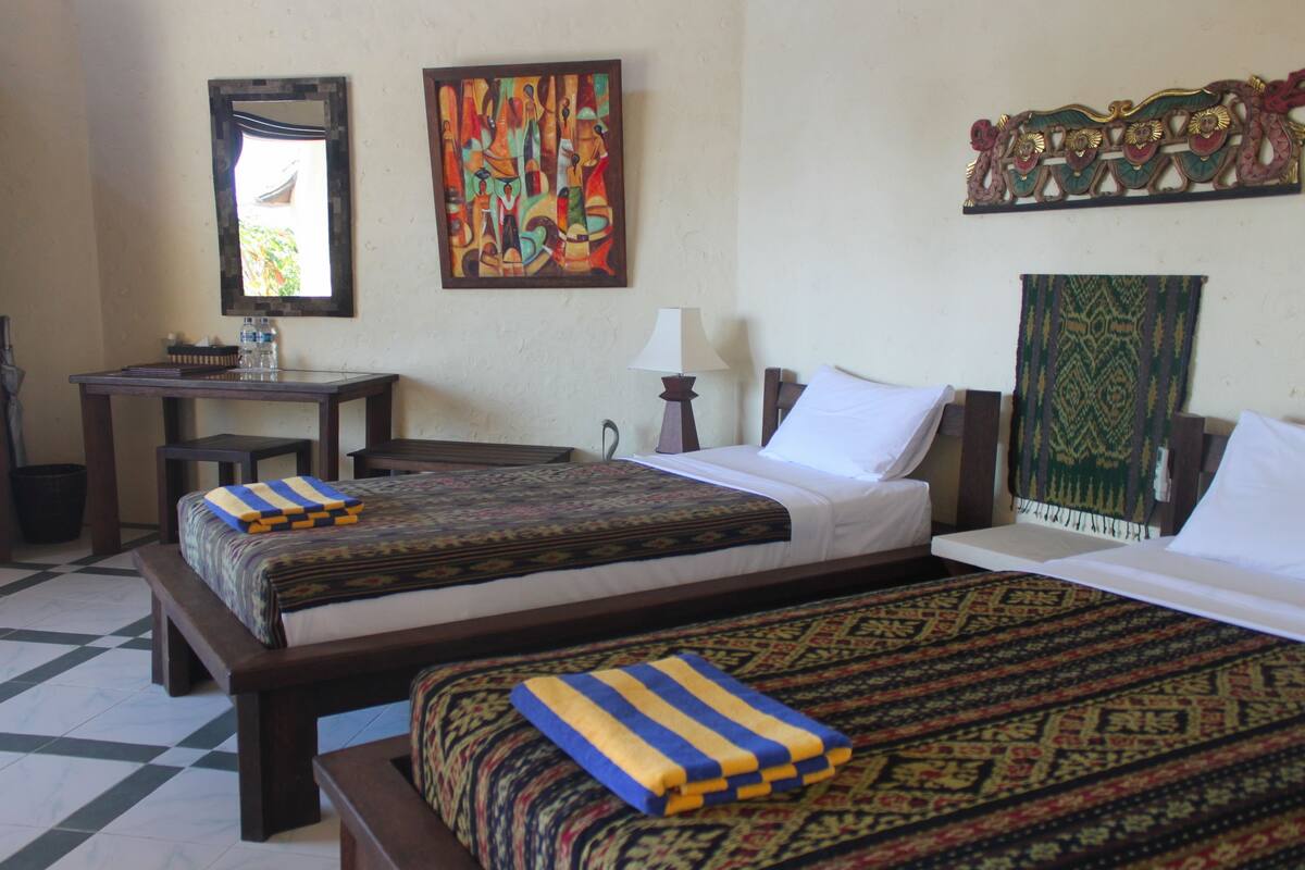A hotel room with two beds, a desk, a chair, a mirror, and a wall with decorative items.