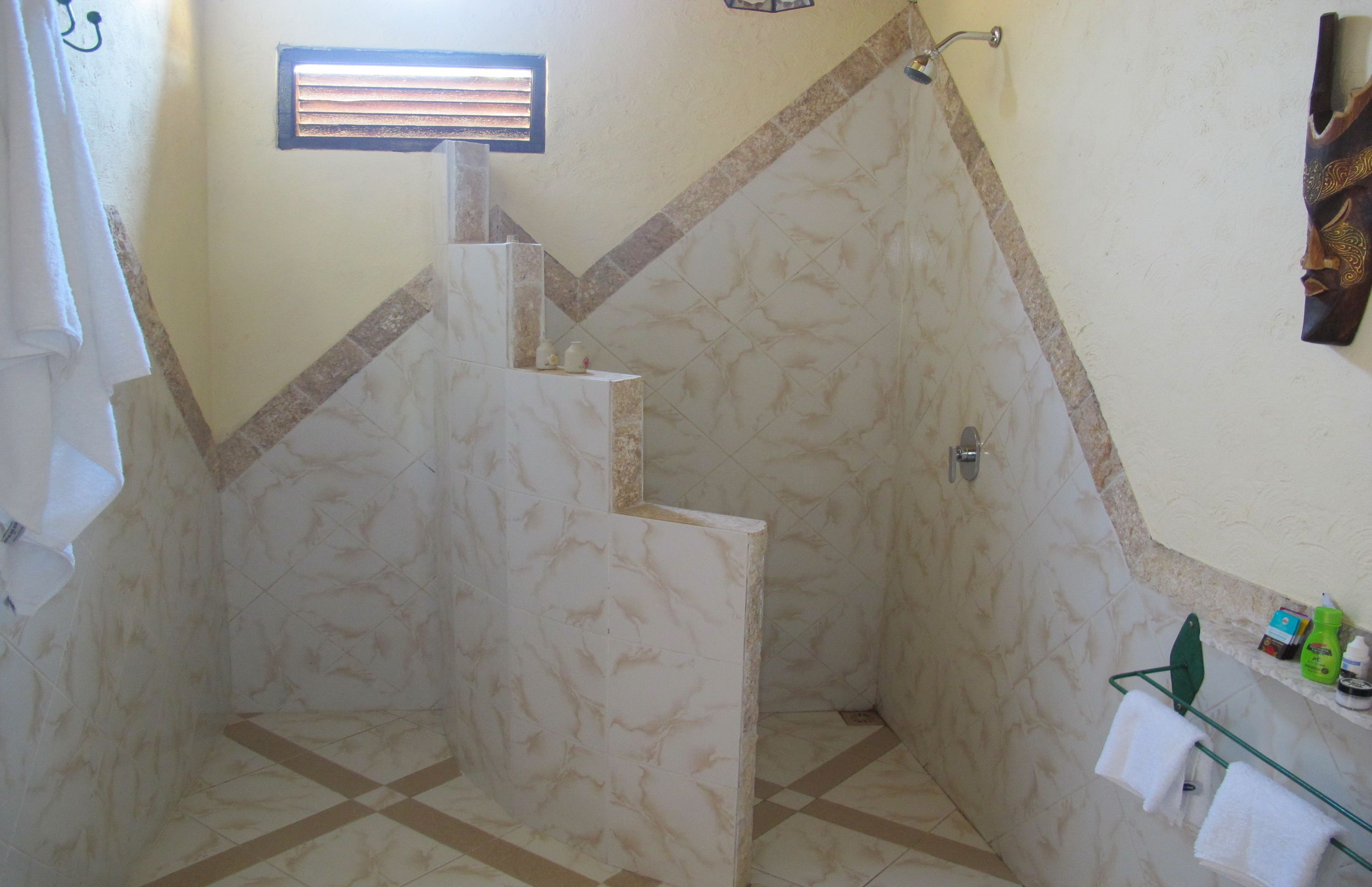 A bathroom with a shower, tiled walls, a towel rack, and a small shelf with toiletries.