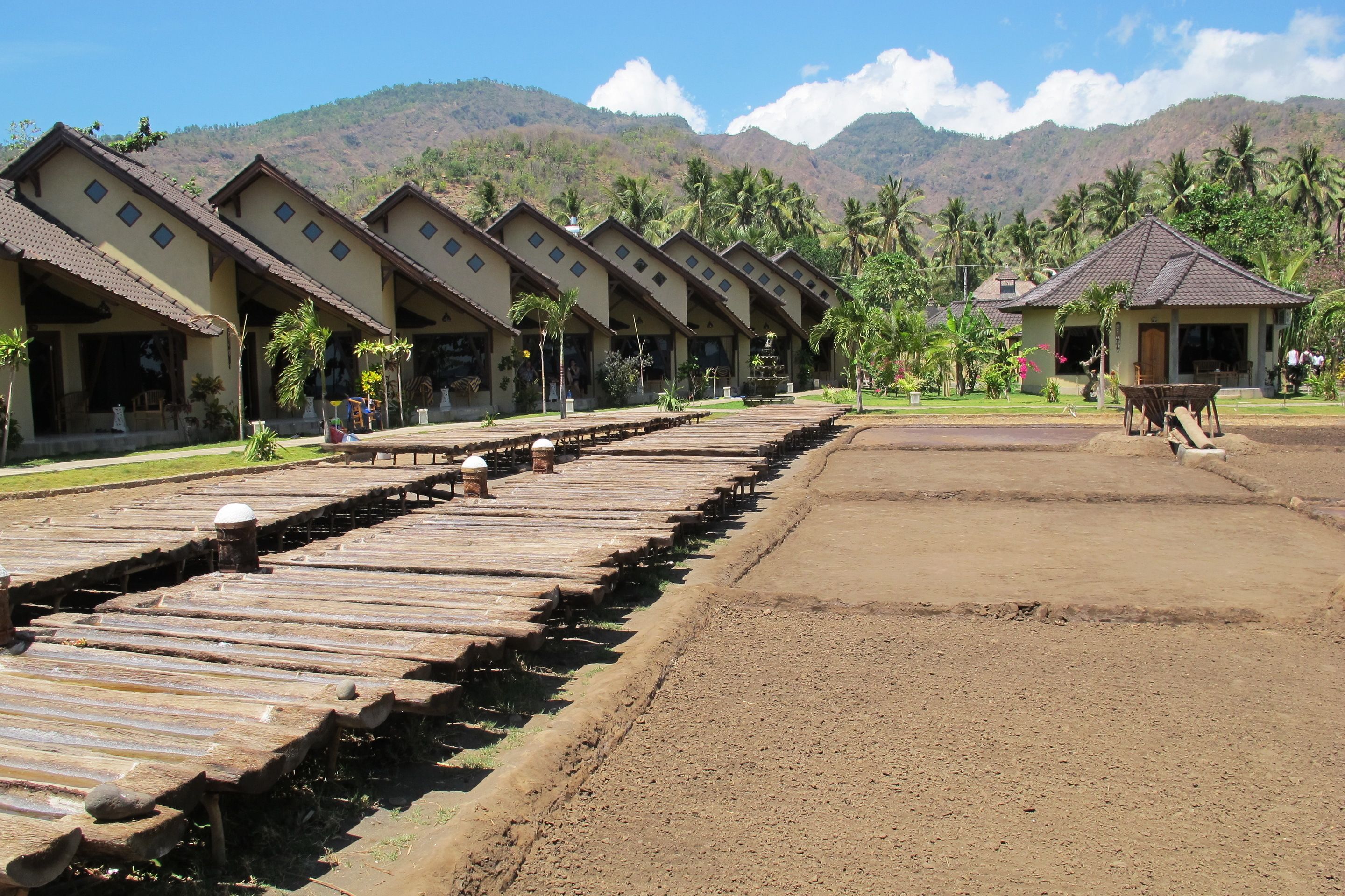Hileras de alojamientos tipo bungalow con suelo de tierra y pasillo de madera.