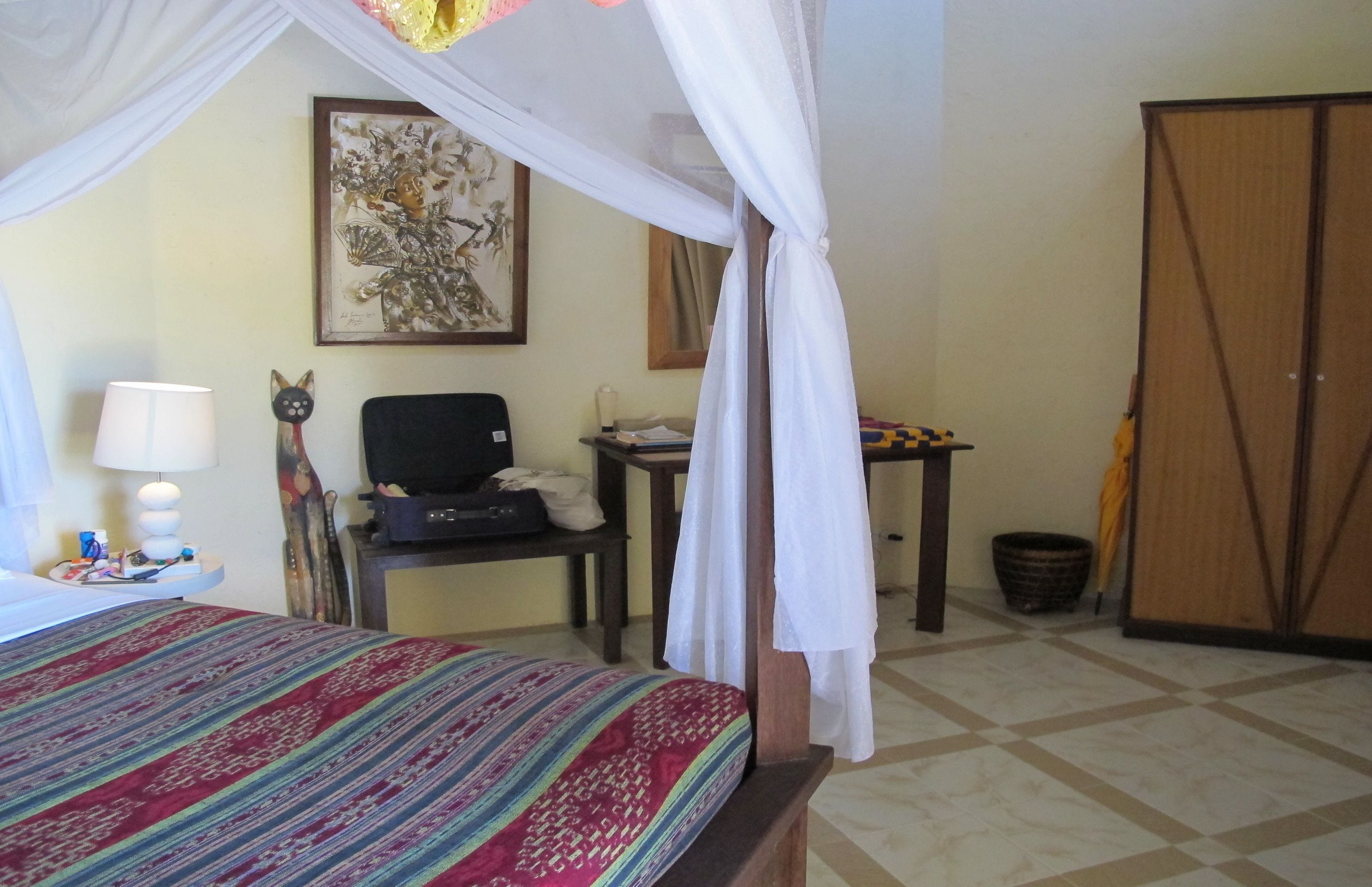 A room with a bed under a canopy, a desk with a chair, a television, and a wardrobe.