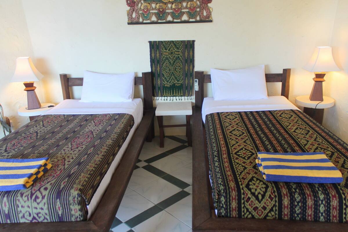 A hotel room with two single beds, a chair, and a decorative wall hanging.