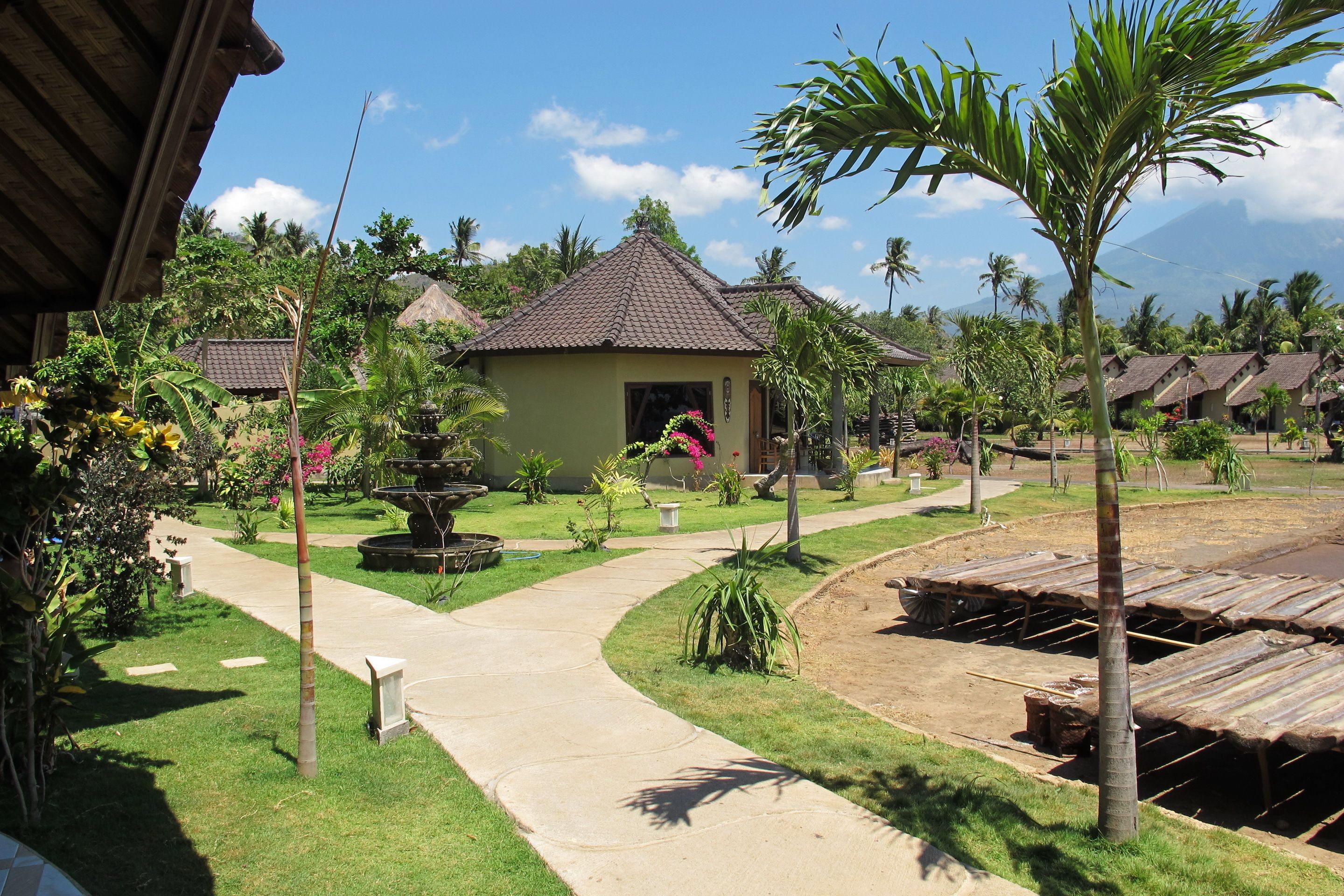 Un resort con cabañas de techo de paja, un jardín central con fuente y una vista despejada del paisaje circundante.