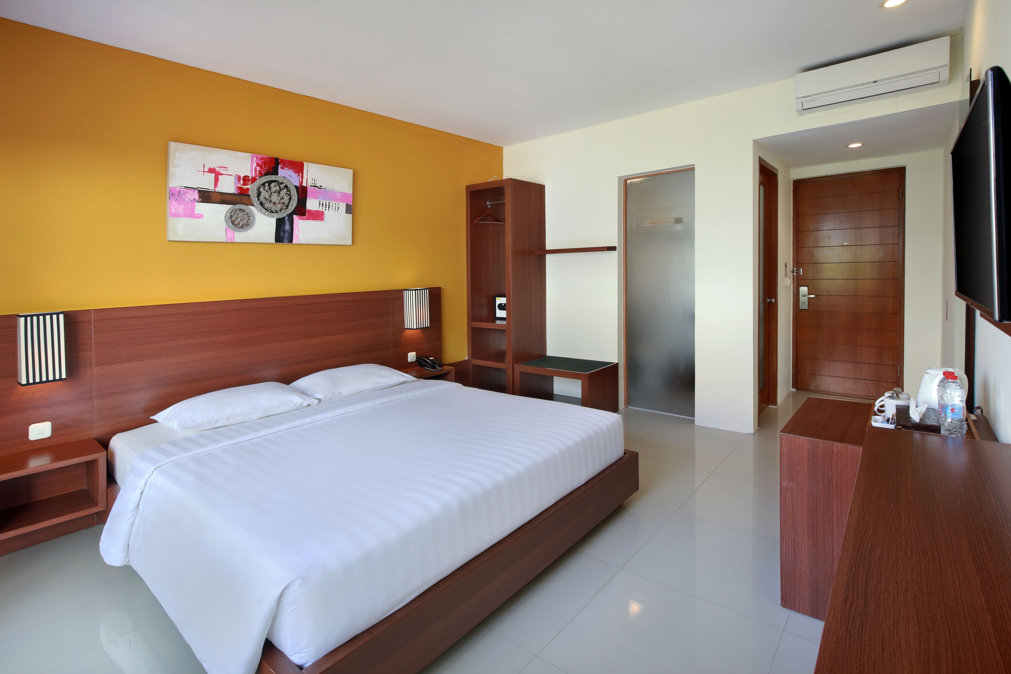 Habitación de hotel con una cama grande, cabecera de madera, mesitas de noche, armario, televisor de pantalla plana y una obra de arte colgada en la pared.