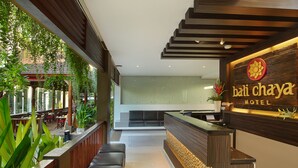 A hotel reception area with a wooden reception desk, a seating area, and a view of the outdoor space. - Bali Chaya Hotel Legian (Legian)