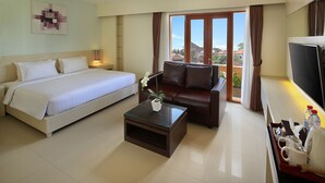 A hotel room with a bed, a sofa, a coffee table, a TV, and a view of the outside. - Bali Chaya Hotel Legian (Legian)