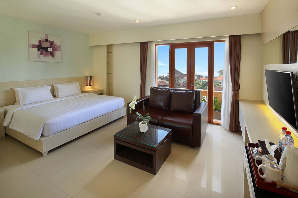 A hotel room with a bed, a sofa, a coffee table, a TV, and a view of the outside.