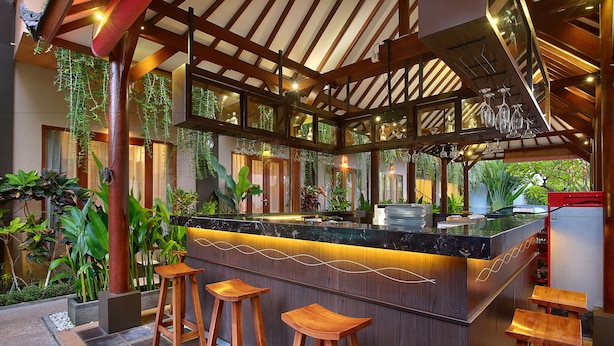 A bar area with a marble countertop, wooden stools, and hanging plants. - Bali Chaya Hotel Legian (Legian)
