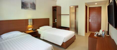 A hotel room with two beds, a desk, a wardrobe, and a television.