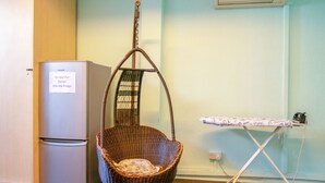 A wicker chair, a small refrigerator, and an ironing board in a room with light green walls. - Vintage Inn @ Clarke Quay - Hostel (Singapore)