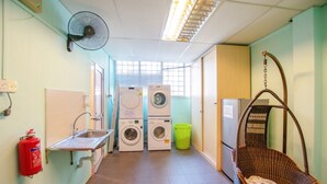 A laundry room with two washing machines, a sink, a fire extinguisher, a hanging basket, and a fan. - Vintage Inn @ Clarke Quay - Hostel (Singapore)
