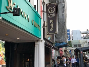 Un edificio con un cartello verde con su scritto "MINA CUPPA" e un cartello nero con "SONG FA bak kut teh" e "DAL 1969".
