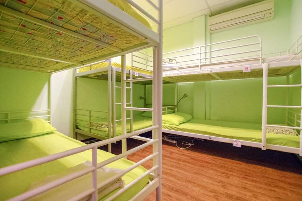 A dormitory room with bunk beds, wooden flooring, and a visible air conditioning unit on the wall.