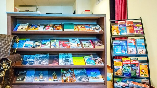 A display of travel books and maps in a room with wooden shelves and a metal rack. - Vintage Inn @ Clarke Quay - Hostel (Singapore)