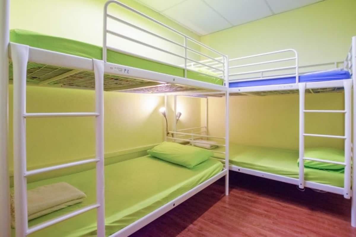 A bunk bed room with green bedding and a wooden floor.