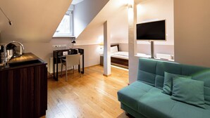 Un dormitorio tipo loft moderno con piso de madera, un sofá verde, un escritorio y un televisor montado en la pared.