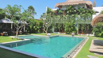 A rectangular pool with clear blue water, surrounded by well-maintained grass and a stone border.