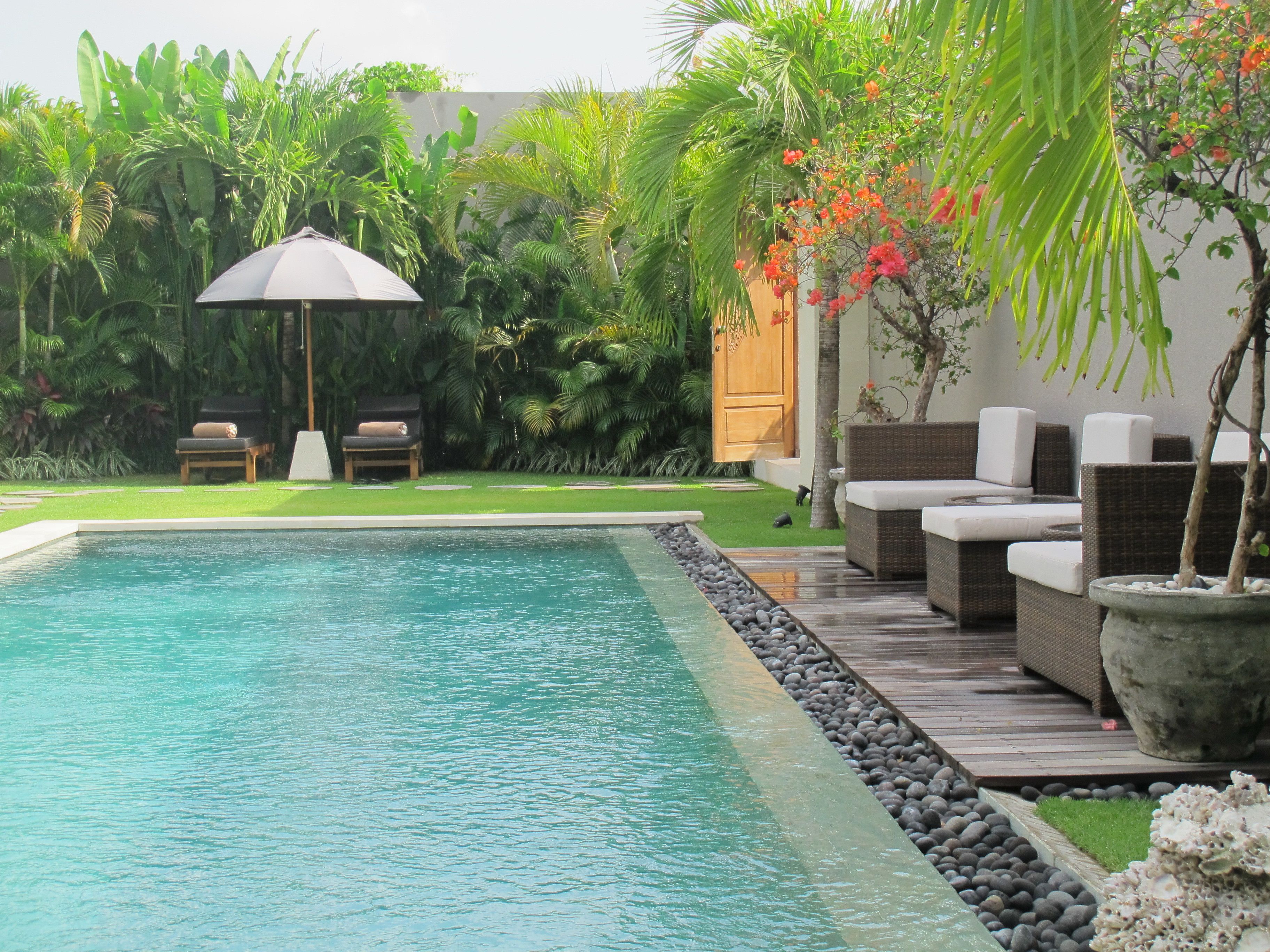 A pool with a wooden deck, lounge chairs, and a wooden door.