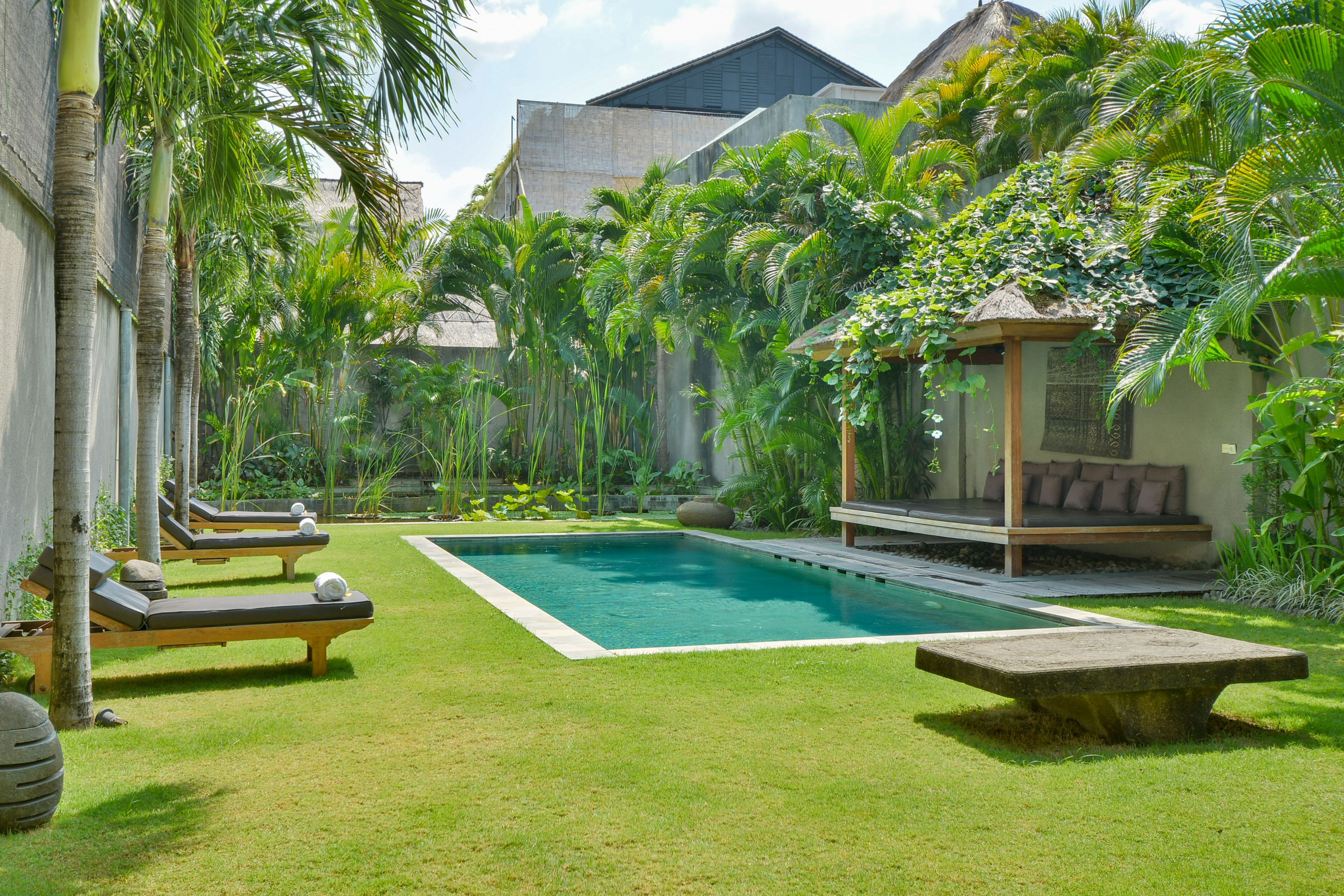 A pool area with lounge chairs, a small deck, and lush tropical vegetation.