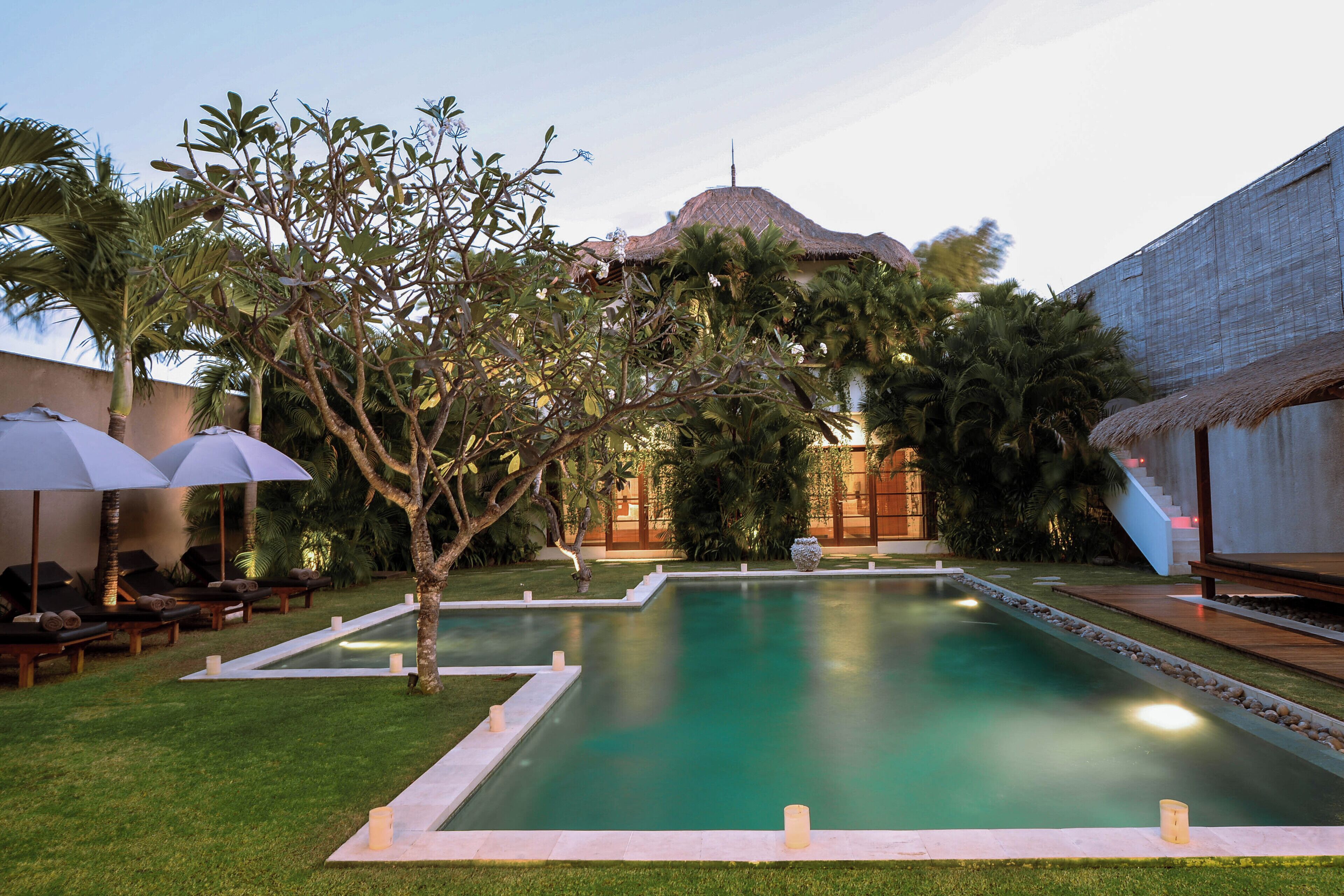 A swimming pool with a surrounding garden, lounge chairs, and umbrellas.