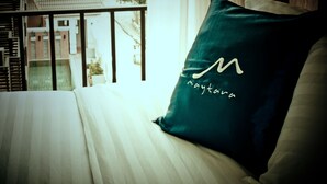 Ein Bett mit weißer Bettdecke und einem türkisfarbenen Kopfkissen mit einem Monogramm.