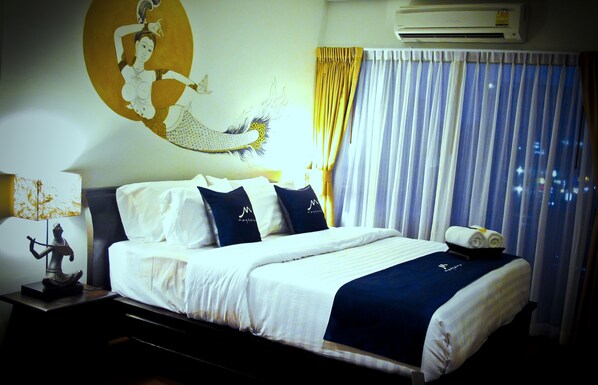 A neatly made bed with a blue and white bedspread, a pillow with a logo, and a decorative statue on the nightstand.