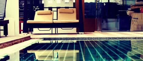 A modern pool area with a glass enclosure, lounge chairs, and a covered seating area.
