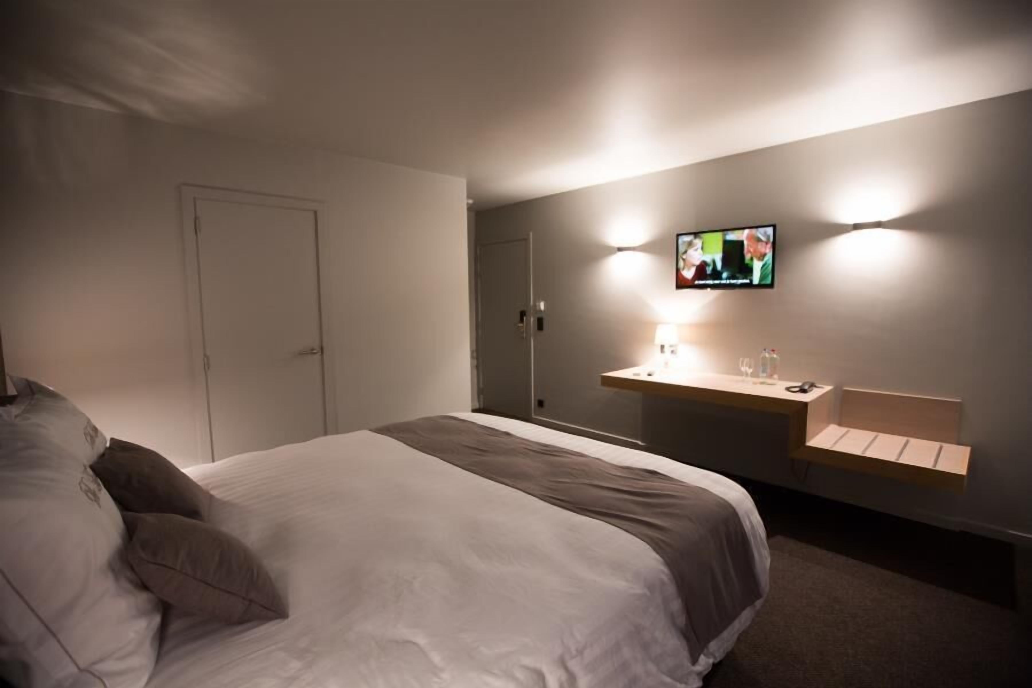 Une chambre d’hôtel avec un lit, une table de chevet avec une lampe et un téléviseur fixé au mur.