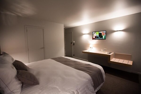 Ett hotellrum med en säng, ett sängbord med en lampa och en tv som är monterad på väggen.