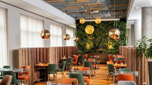 Un restaurante con mesas de madera, sillas verdes y anaranjadas, y lámparas esféricas colgantes.