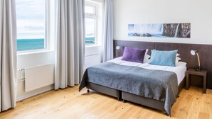 Un dormitorio con cama, vista al mar, un cuadro en la pared y una mesita de noche con lámpara.