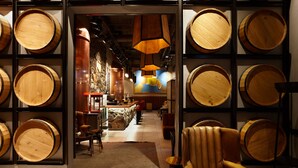 Zona de bar con barriles de madera, sillones de cuero y un fondo de pared de piedra.