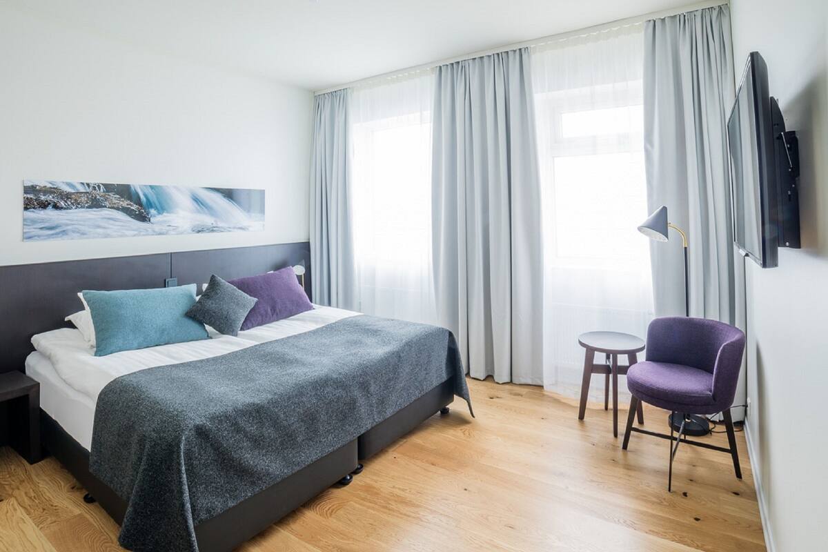 Et moderne hotelværelse med seng, stol, fjernsyn og et maleri på væggen.