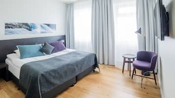 A modern hotel room with a bed, a chair, a TV, and a painting on the wall.