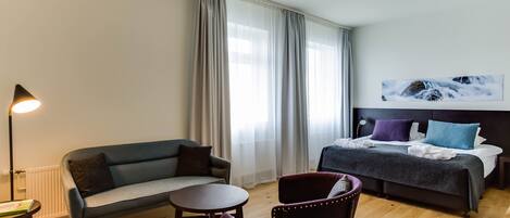 A modern hotel room with a bed, a sofa, a small table, and two chairs.