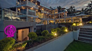 A modern multi-story building with a glass facade, outdoor seating, and a neon sign. - Levels Unawatuna (Unawatuna)