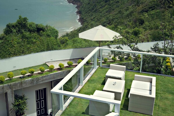 A rooftop terrace with outdoor furniture, a white umbrella, and a view of the coastline.