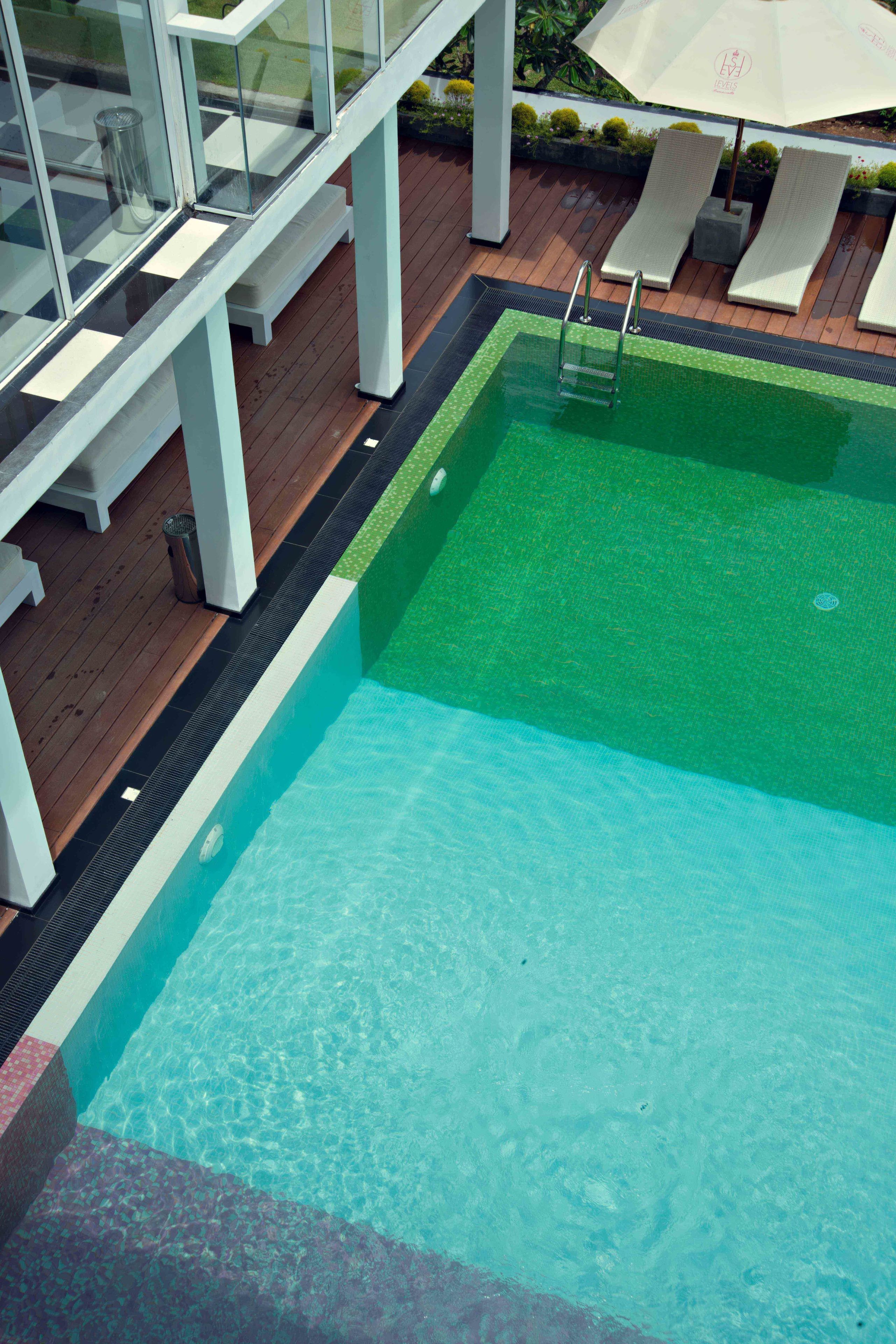 A swimming pool with a clear blue water, surrounded by wooden deck and white lounge chairs.