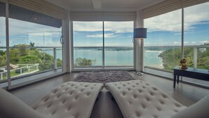 A modern room with large windows offering a view of a body of water and greenery. There are two tufted sofas and a floor lamp. - Levels Unawatuna (Unawatuna)
