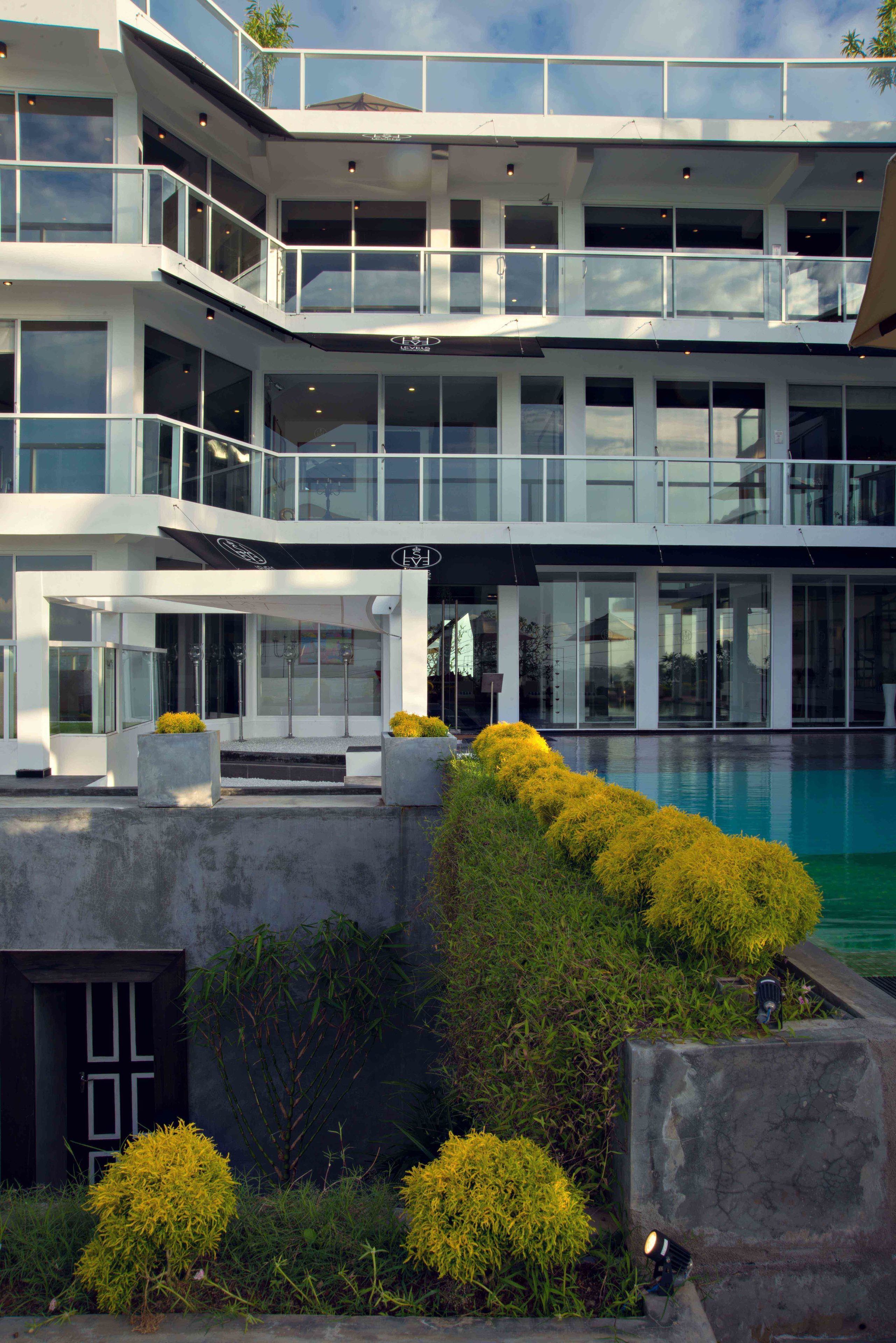 A multi-story building with a pool, large windows, and outdoor seating areas.