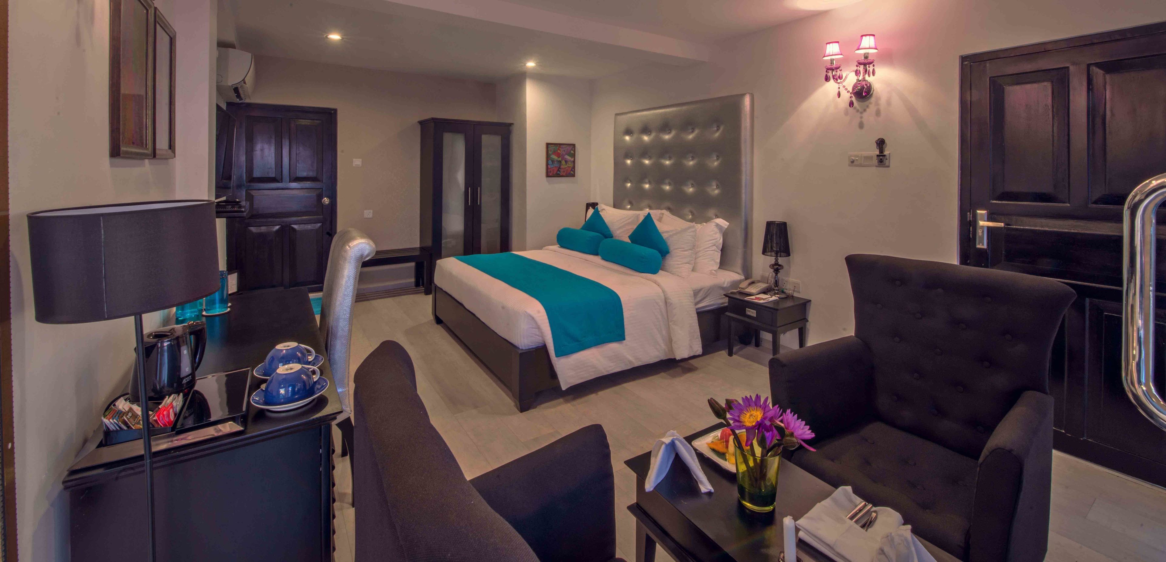 Habitación de hotel con cama, zona de estar con sofá y sillones, escritorio con lámpara, estación de café y baño a la vista.
