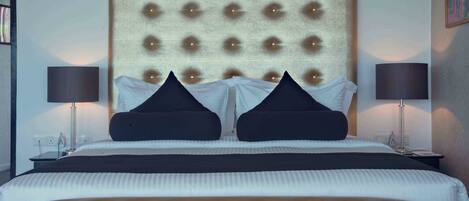 A hotel room with a tufted headboard, two black accent pillows, a white bedspread, and two bedside lamps.