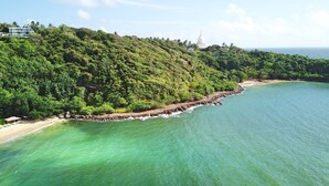 A coastal landscape with a beach, rocky shoreline, and a hill with dense vegetation and a white dome structure. - Levels Unawatuna (Unawatuna)