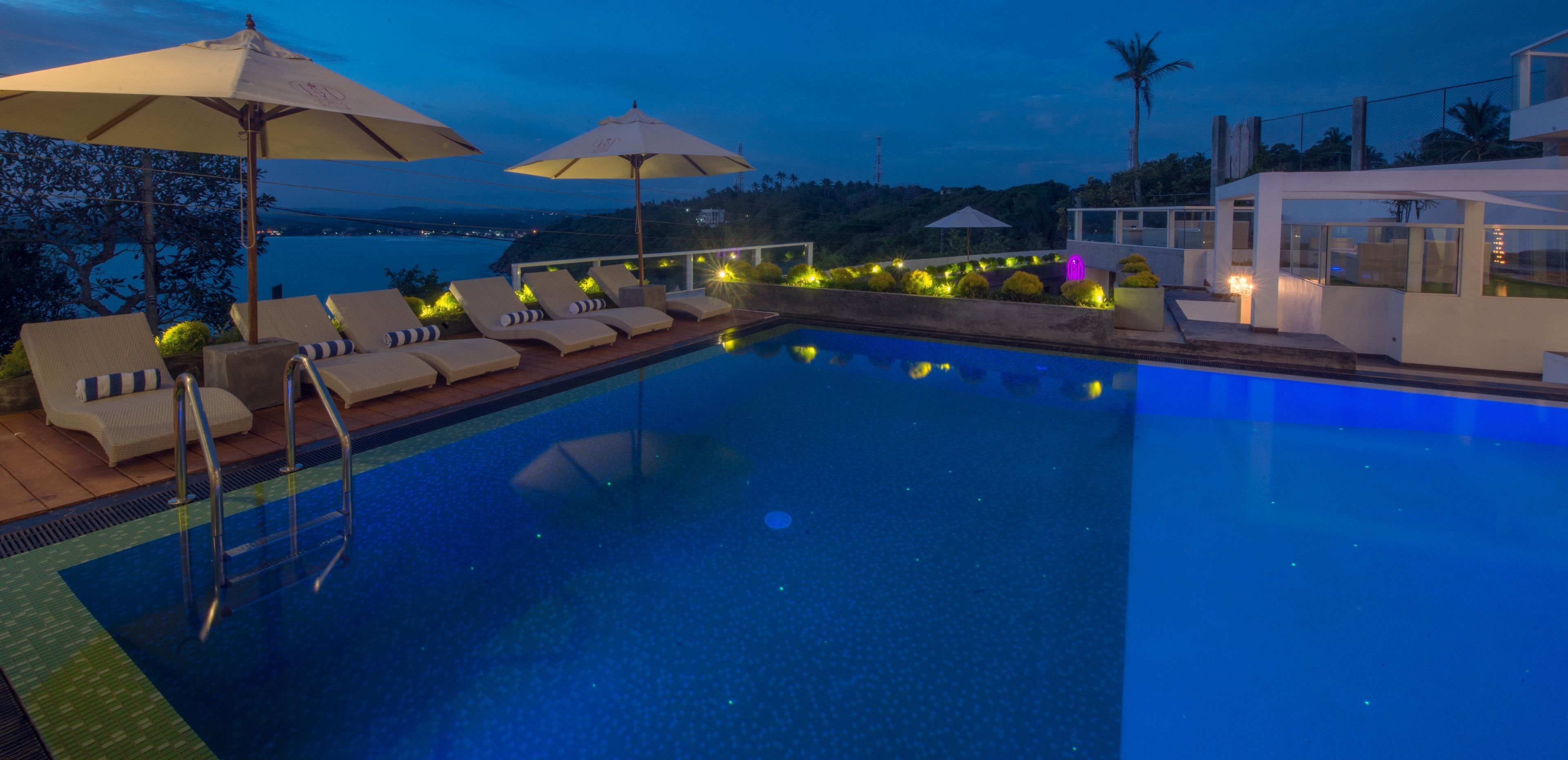 Un espace aménagé au bord de la piscine, avec des chaises longues et des parasols, une piscine et une vue sur la mer.